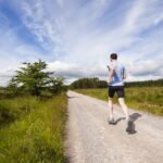 A person running on a road beside a grass field
