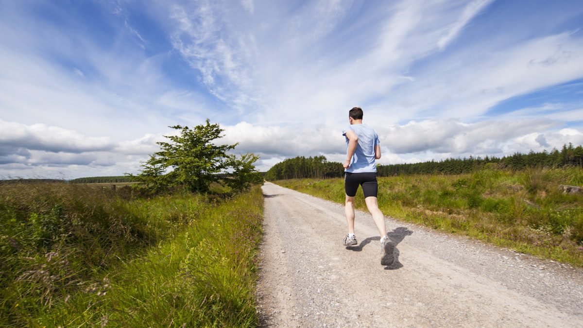 A person running on a road beside a grass field